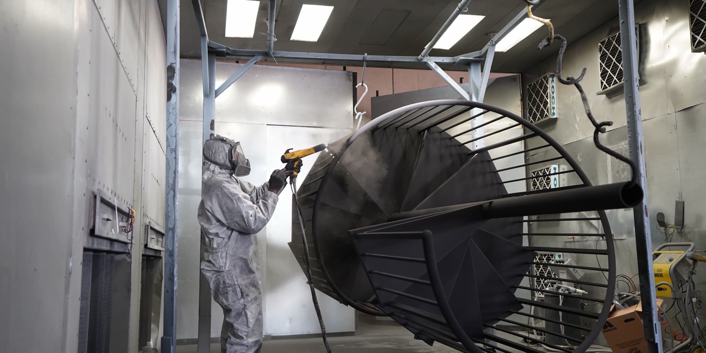 Technician powder coating a metal part in a spray booth